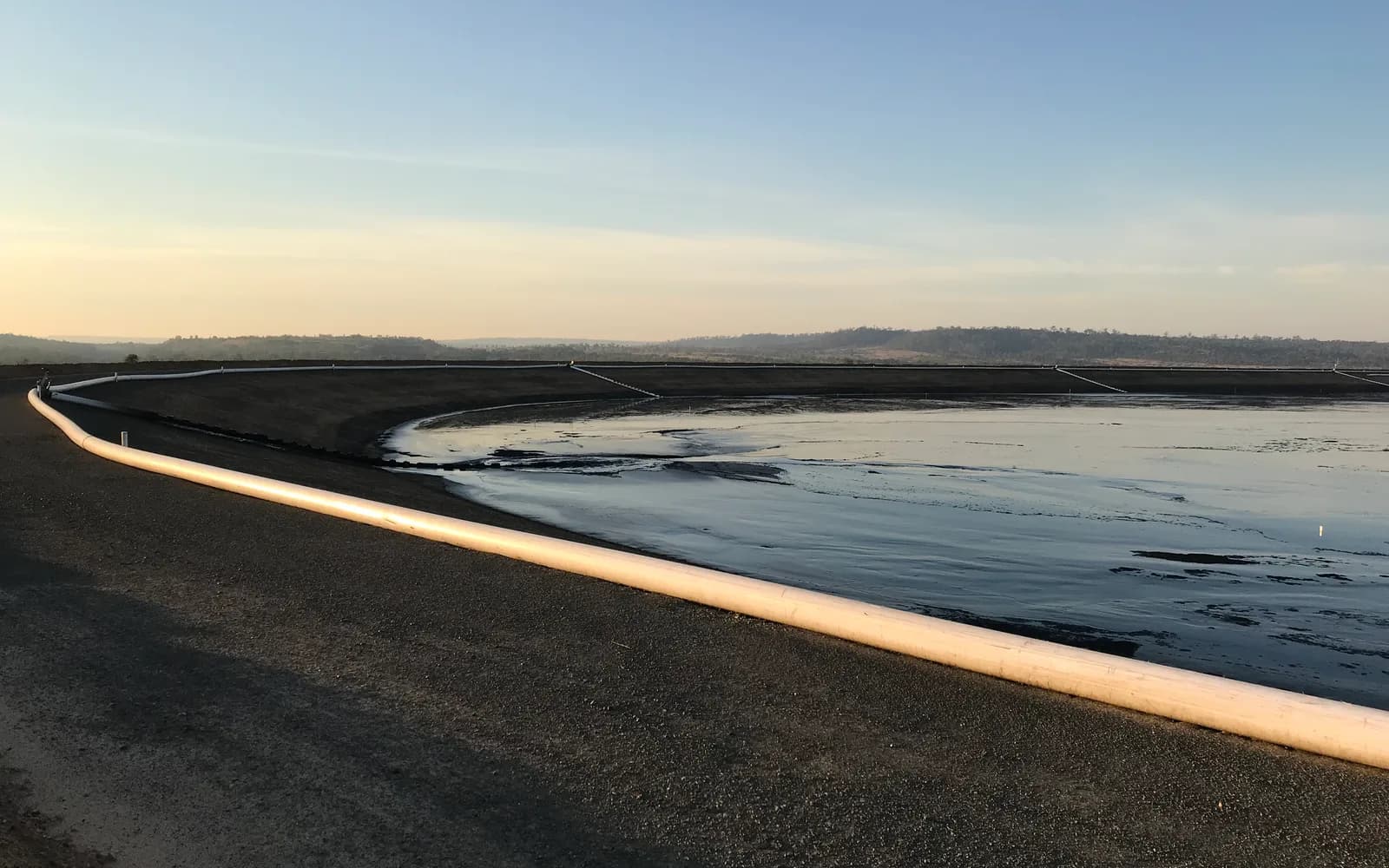 Tailings pipeline along the crest of the tailings dam at Blackwater Mine during the 2018 raise, at dawn, with the tailings beach and pond beyond