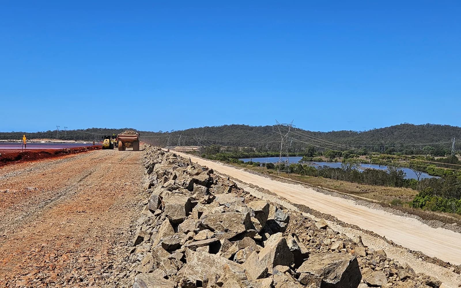 Rock-armoured crest of the raised tailings storage facility embankment at the QAL refinery, Gladstone, with the tailings pond beside it