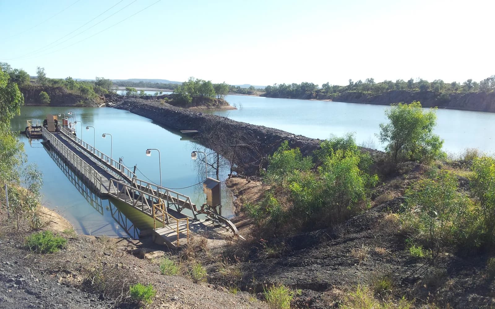 Mine water storage at Saraji Mine with a floating pump pontoon, lit walkway and rock-armoured dividing embankment