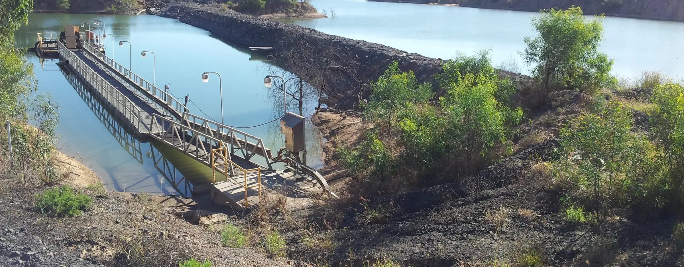 Mine water storage with a floating pump pontoon, lit walkway and rock-armoured dividing embankment