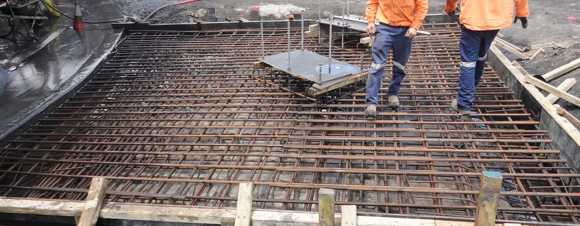 Reinforcement cage for a slab with a cast-in plate, two workers checking the steel before the pour