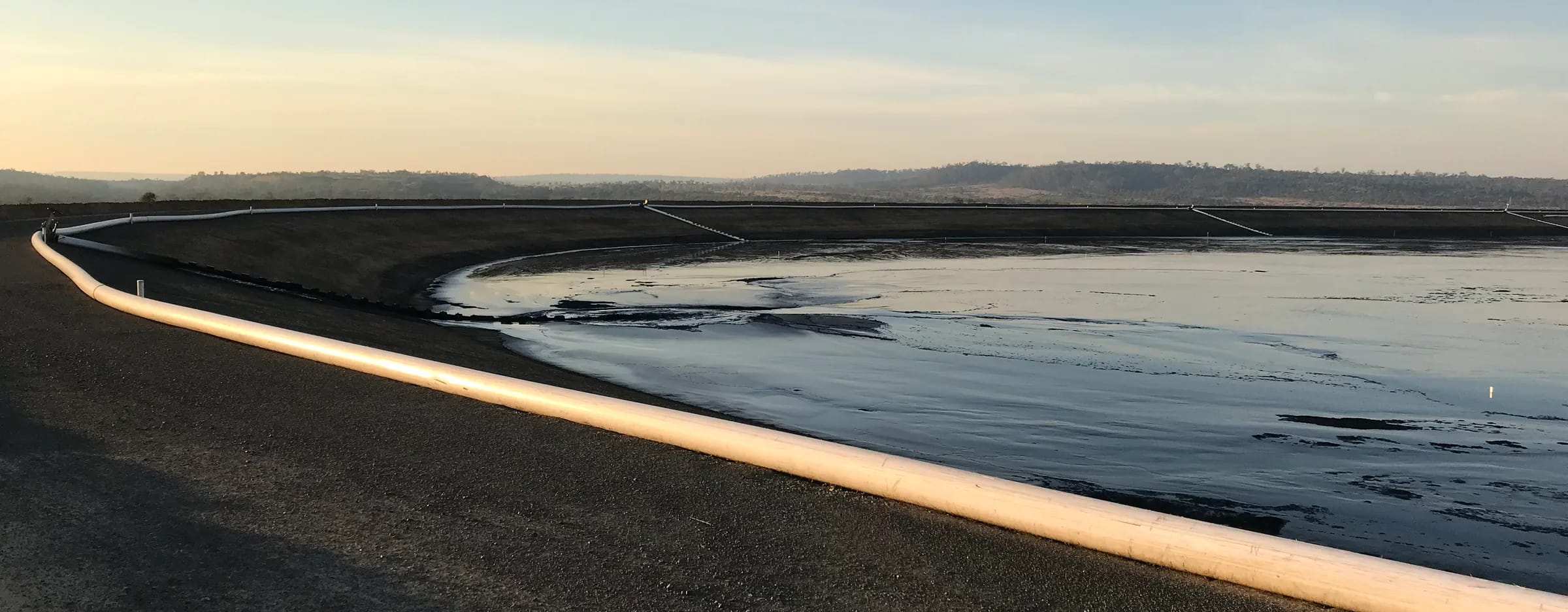 Tailings pipeline along the crest of the tailings dam at Blackwater Mine during the 2018 raise, at dawn, with the tailings beach and pond beyond
