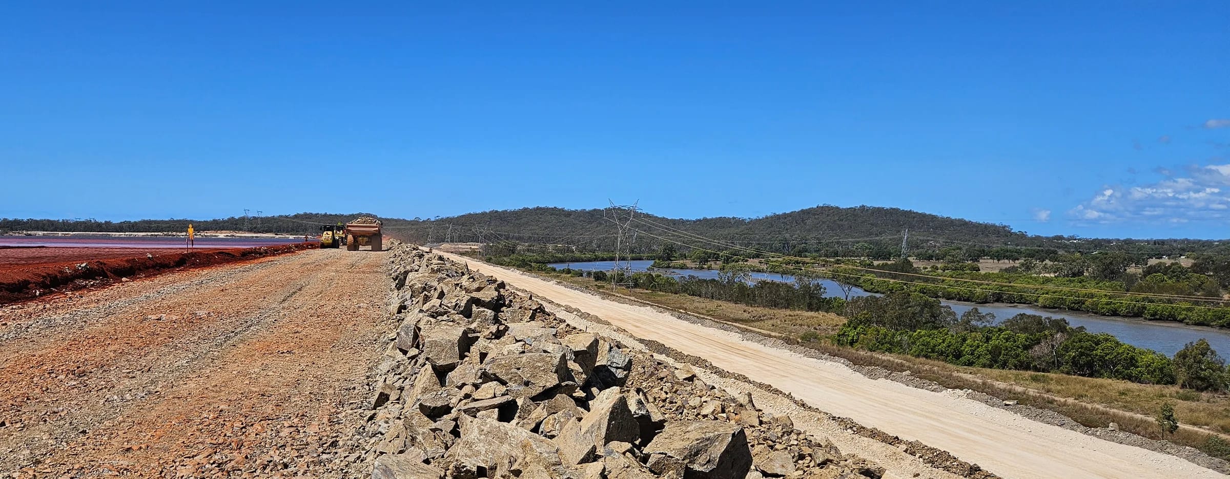 Rock-armoured crest of the raised tailings storage facility embankment at the QAL refinery, Gladstone, with the tailings pond beside it